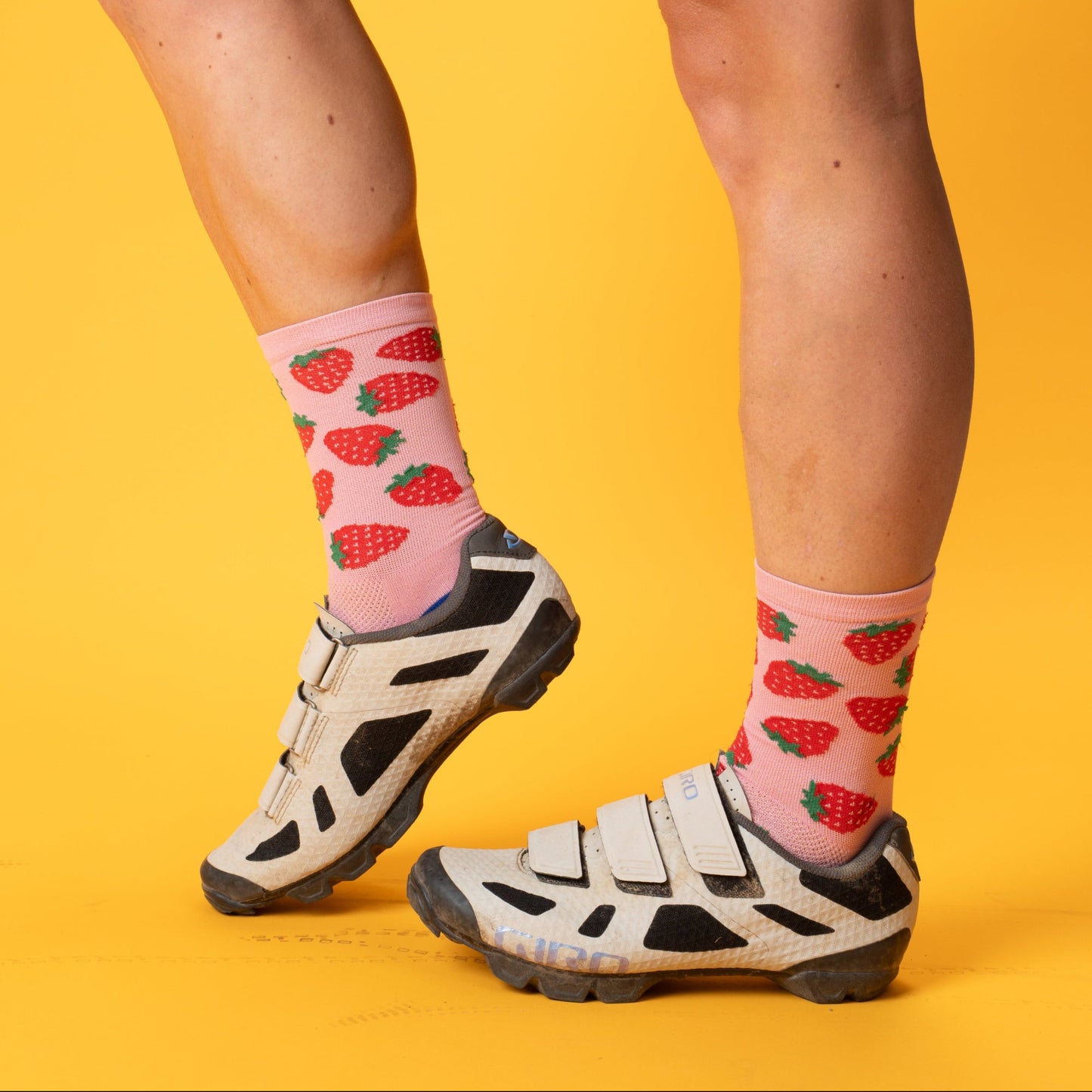 Person wearing black cycling shorts and strawberry-patterned socks on a yellow background